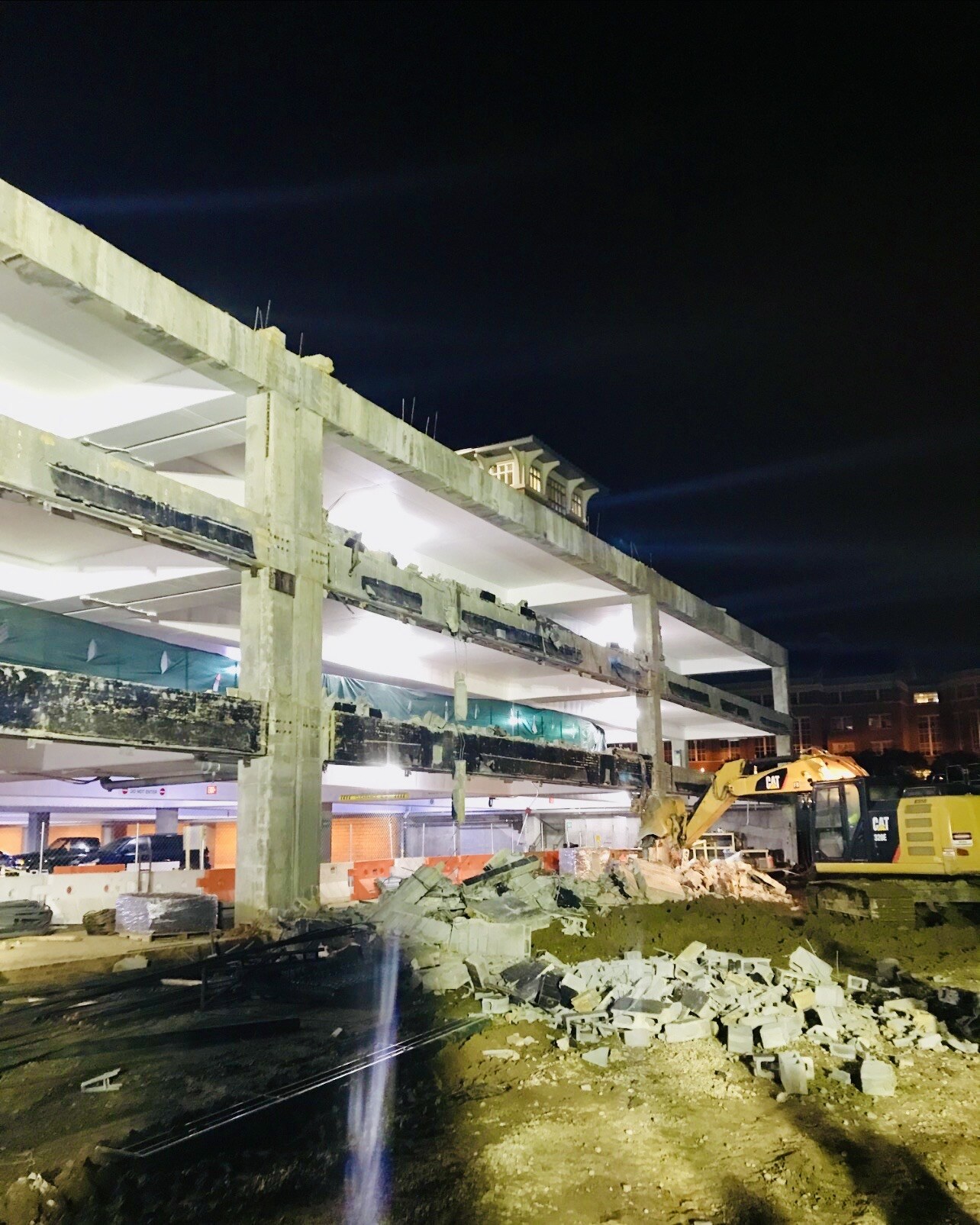 Excavator performing nighttime demolition beside an exposed concrete structure